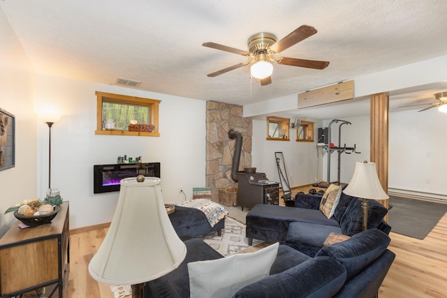 247 Daylily Ct, Terra Alta, WV 26764 - living room featuring a wood stove, a ceiling fan, wood finished floors, a textured ceiling, and a baseboard radiator