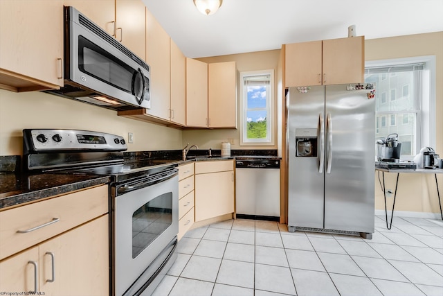 kitchen featuring stainless steel appliances, a sink, light brown cabinets, light tile patterned flooring, and dark stone counters