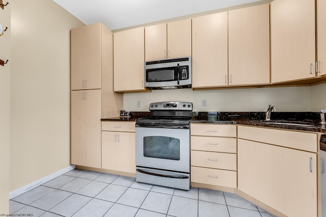 kitchen featuring stainless steel appliances, cream cabinets, a sink, dark stone counters, and light tile patterned flooring