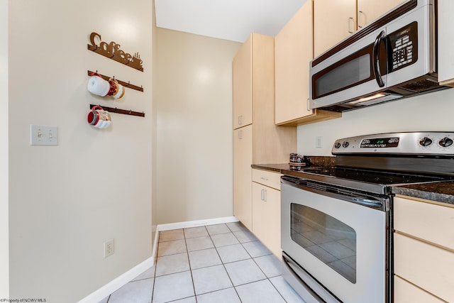 kitchen featuring stainless steel appliances, dark countertops, light tile patterned floors, and baseboards