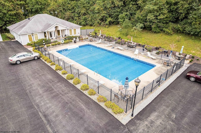 community pool with fence, a view of trees, and a patio area