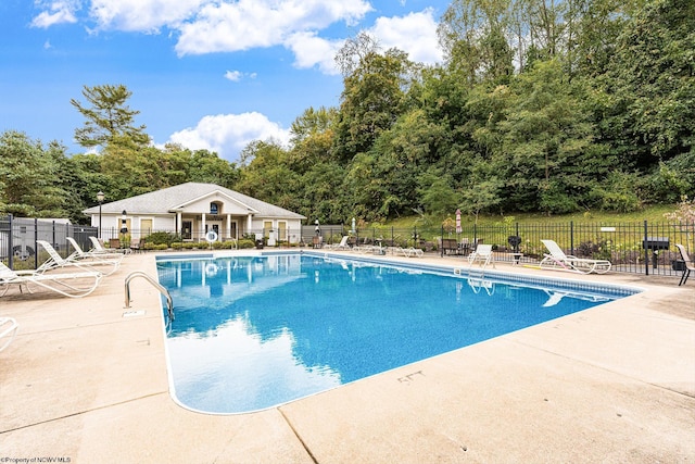 community pool featuring fence, a patio, and view of scattered trees