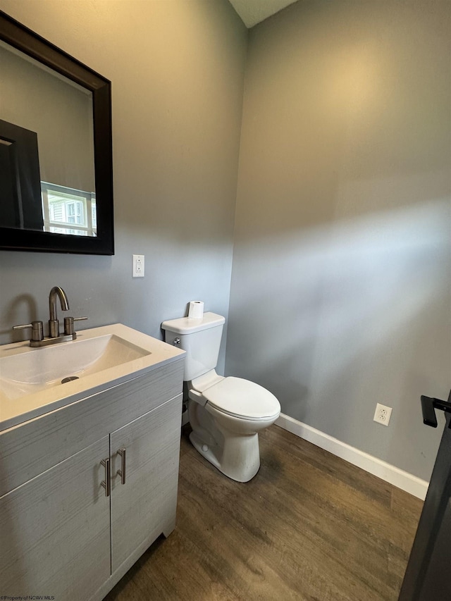half bath featuring wood finished floors, toilet, vanity, and baseboards