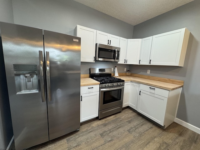 kitchen featuring appliances with stainless steel finishes, dark wood-style floors, wood counters, white cabinets, and a textured ceiling