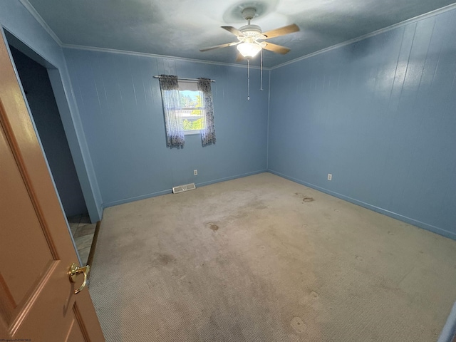 empty room featuring a ceiling fan, crown molding, light colored carpet, and baseboards