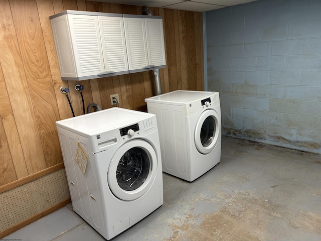 laundry room featuring washer and clothes dryer, concrete block wall, wood walls, and cabinet space