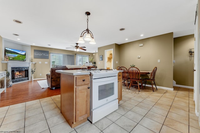 kitchen featuring white gas range, open floor plan, a kitchen island, a lit fireplace, and light tile patterned floors