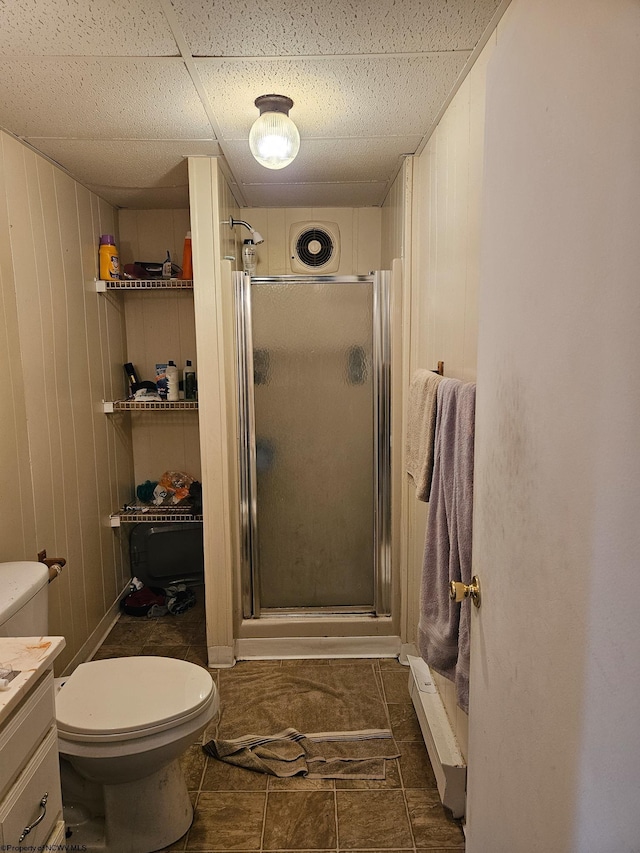 full bathroom with a shower stall, toilet, vanity, a drop ceiling, and wooden walls