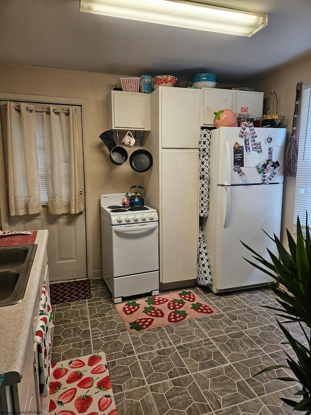 kitchen featuring white appliances, a sink, dark stone finish flooring, light countertops, and white cabinets