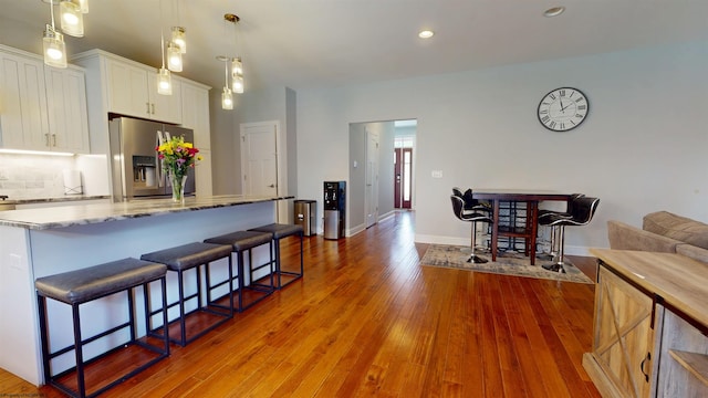 123 Sadie Ln, Morgantown, WV 26508 - kitchen with stainless steel fridge with ice dispenser, white cabinets, wood finished floors, a breakfast bar, and light stone counters