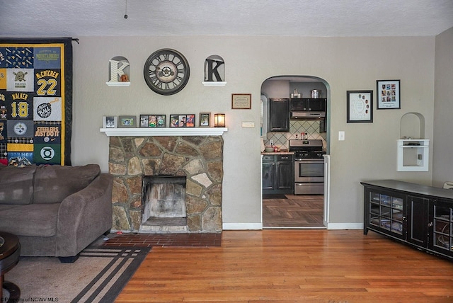 1917 Pleasant Valley Rd, Fairmont, WV 26554 - living room with arched walkways, wood finished floors, a textured ceiling, a stone fireplace, and baseboards