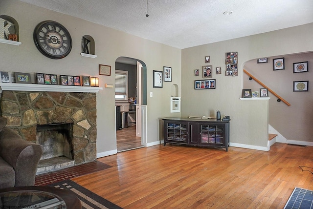1917 Pleasant Valley Rd, Fairmont, WV 26554 - living room featuring arched walkways, hardwood / wood-style floors, a stone fireplace, a textured ceiling, and baseboards