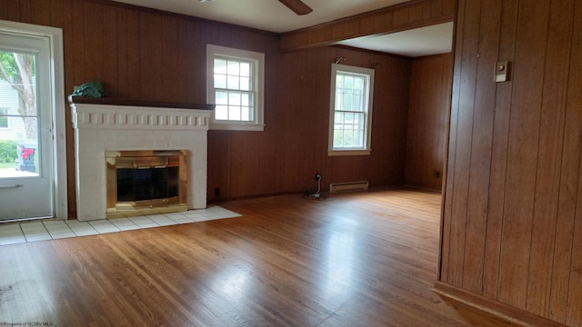 110 15th St, Elkins, WV 26241 - unfurnished living room featuring baseboard heating, light wood-type flooring, a fireplace, ceiling fan, and wood walls
