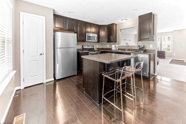 126 Auburn Dr, Morgantown, WV 26501 - kitchen featuring appliances with stainless steel finishes, dark brown cabinetry, a kitchen island, a breakfast bar, and dark wood-style floors