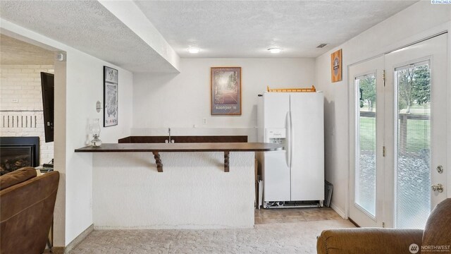 863 S Meadowlark Ln, Othello, WA 99344 - kitchen with white refrigerator with ice dispenser, a textured ceiling, baseboards, a breakfast bar, and a brick fireplace