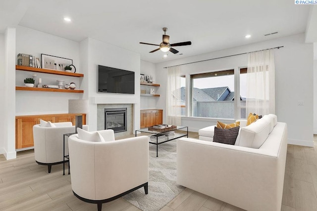 living room with ceiling fan, a tiled fireplace, and light wood-type flooring