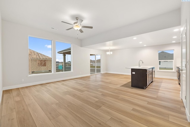 unfurnished living room with ceiling fan with notable chandelier, sink, and light wood-type flooring