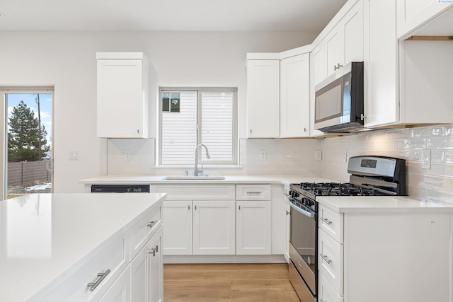 kitchen featuring light countertops, a sink, light wood-style flooring, appliances with stainless steel finishes, and backsplash