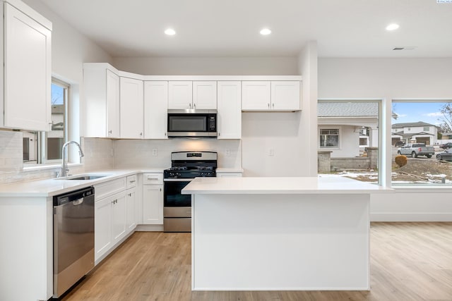kitchen featuring a sink, white cabinets, stainless steel appliances, and light wood finished floors