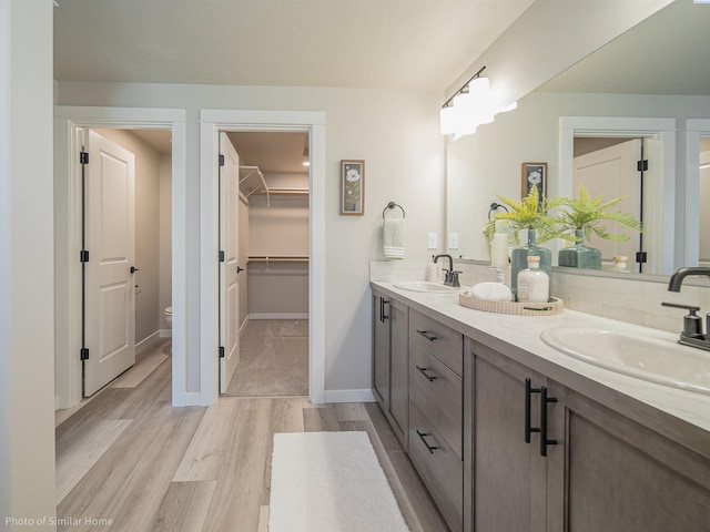 full bathroom featuring wood finished floors, a sink, toilet, and double vanity