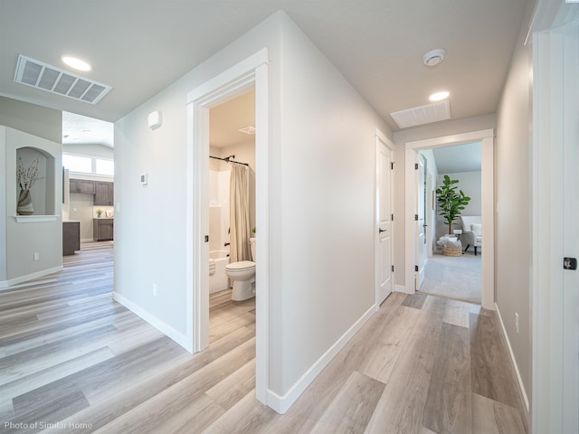 corridor with light wood-style flooring, visible vents, baseboards, and a barn door