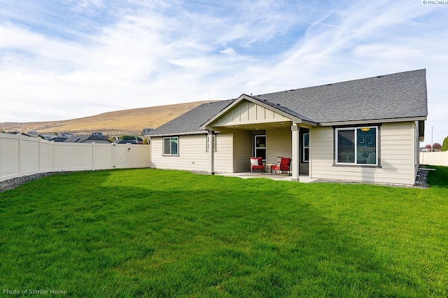 rear view of house featuring a shingled roof, a fenced backyard, a yard, a patio area, and board and batten siding