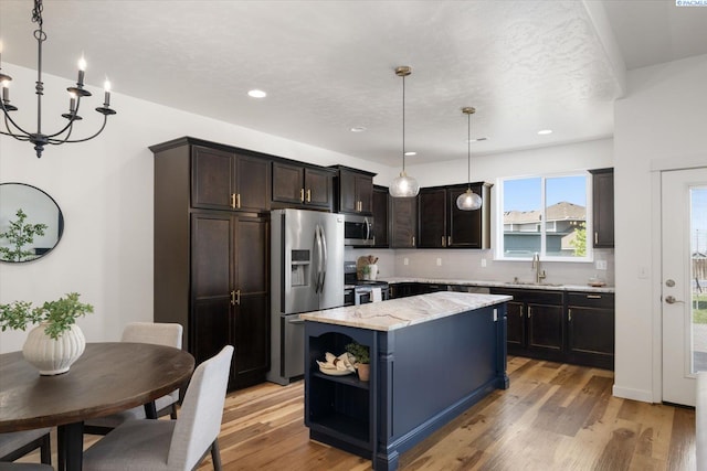 882 Pikes Peak Dr, West Richland, WA 99353 - kitchen with stainless steel appliances, a sink, a kitchen island, light stone countertops, and light wood finished floors
