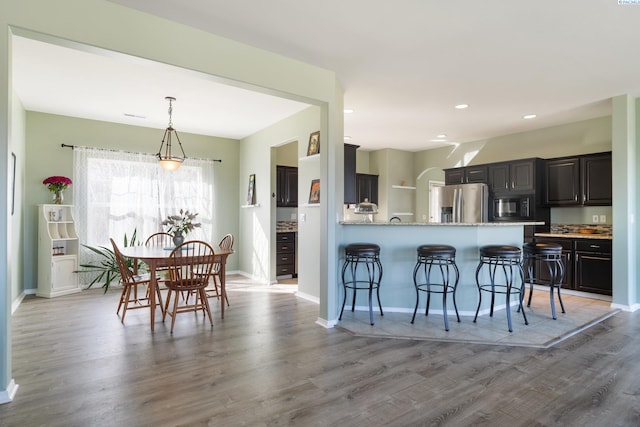 kitchen with a breakfast bar, stainless steel fridge with ice dispenser, light wood-style flooring, black microwave, and baseboards