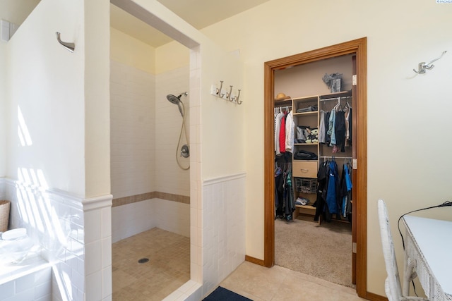 bathroom with tile patterned flooring, a walk in closet, and tiled shower