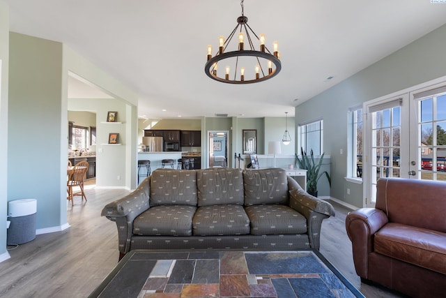 living room featuring an inviting chandelier, baseboards, wood finished floors, and french doors