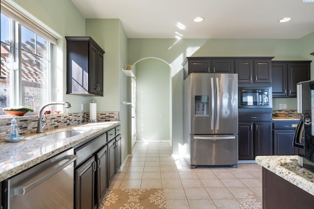 kitchen featuring light tile patterned floors, arched walkways, decorative backsplash, stainless steel appliances, and a sink