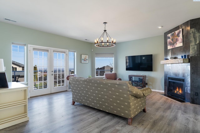 living area with a large fireplace, french doors, wood finished floors, and a notable chandelier