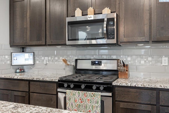 kitchen with appliances with stainless steel finishes, dark brown cabinetry, light stone counters, and tasteful backsplash