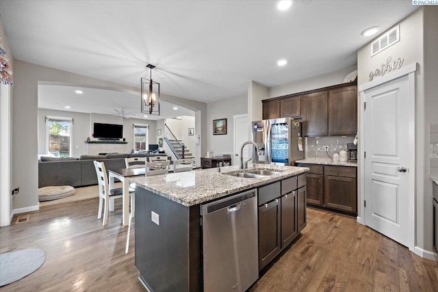 kitchen with visible vents, an island with sink, light stone counters, stainless steel appliances, and dark brown cabinets