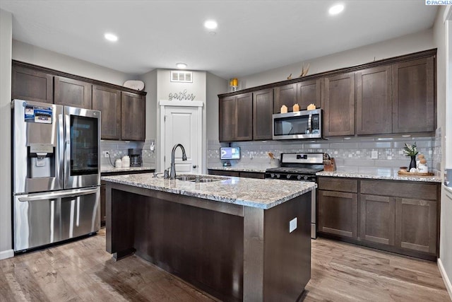 kitchen featuring stainless steel appliances, visible vents, a sink, dark brown cabinetry, and light stone countertops
