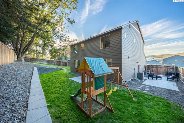 rear view of property featuring a patio, a lawn, a playground, and a fenced backyard