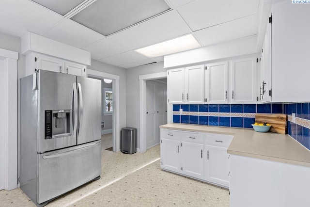 kitchen featuring tasteful backsplash, stainless steel fridge, a drop ceiling, and white cabinets