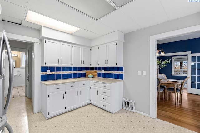 kitchen featuring a drop ceiling, white cabinets, and backsplash