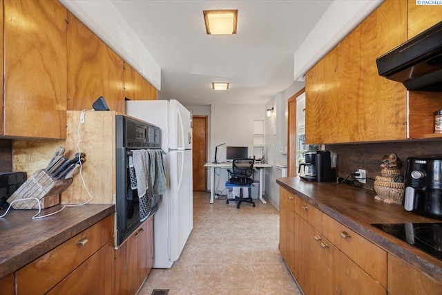 kitchen with under cabinet range hood, brown cabinets, freestanding refrigerator, and wooden counters
