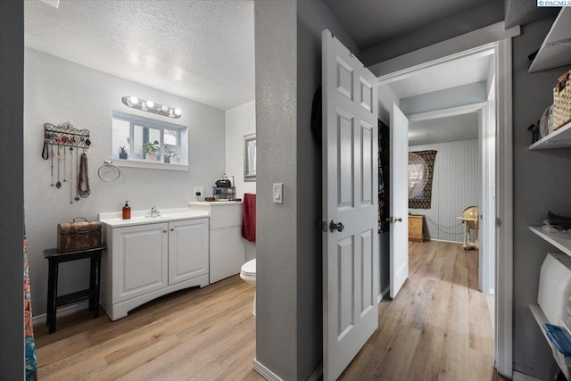 bathroom featuring toilet, vanity, wood finished floors, and a textured ceiling