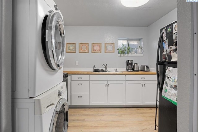 laundry area with light wood finished floors, laundry area, stacked washer and clothes dryer, and a sink