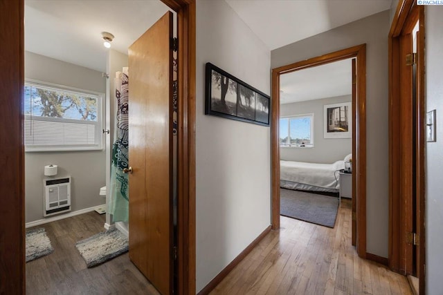 hall featuring light wood-style flooring, baseboards, and heating unit