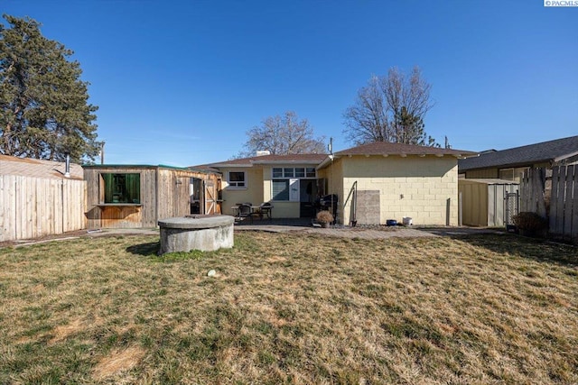 back of house featuring concrete block siding, fence, an outdoor structure, and a lawn