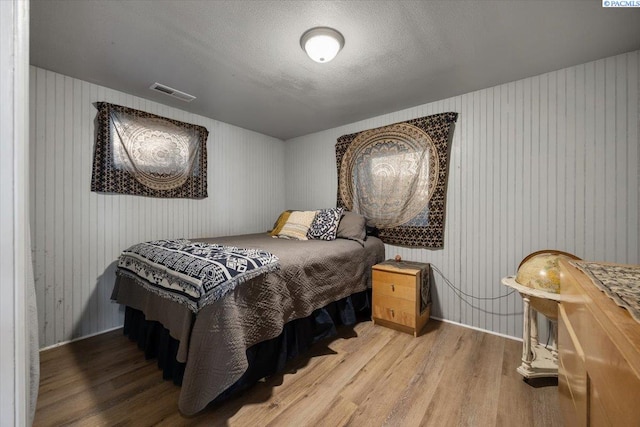 bedroom with wooden walls, visible vents, baseboards, and wood finished floors