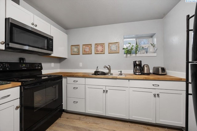 kitchen featuring white cabinets, a sink, stainless steel microwave, wood counters, and black range with electric stovetop