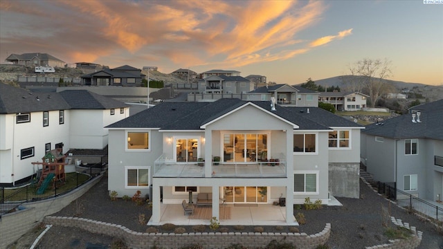 back of property at dusk with a fenced backyard, a balcony, a residential view, stucco siding, and a patio area