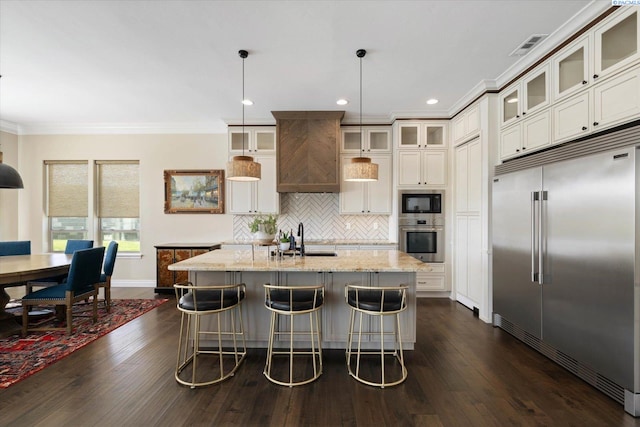 kitchen featuring built in appliances, dark wood finished floors, crown molding, light stone counters, and a sink
