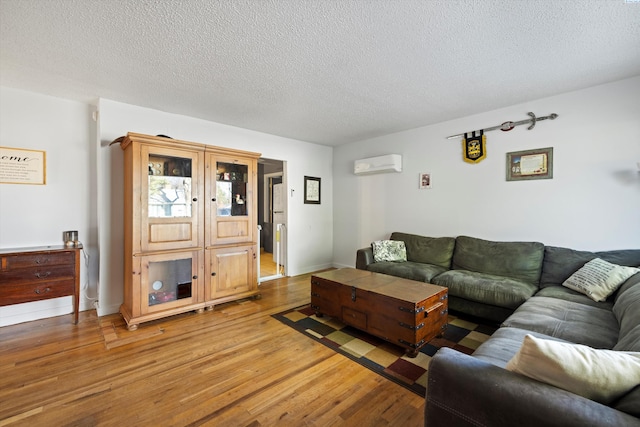 living room with a wall mounted air conditioner, hardwood / wood-style floors, and a textured ceiling