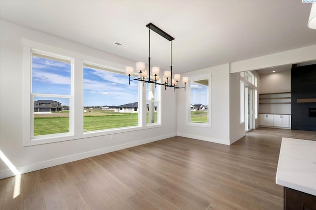unfurnished dining area with wood finished floors, an inviting chandelier, baseboards, and visible vents
