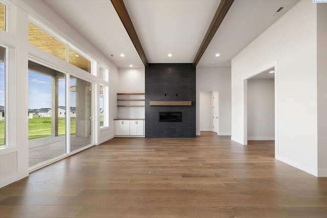 unfurnished living room with baseboards, a tiled fireplace, beam ceiling, recessed lighting, and wood finished floors